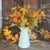 White pitcher with autumn-themed flowers and leaves on a wooden surface